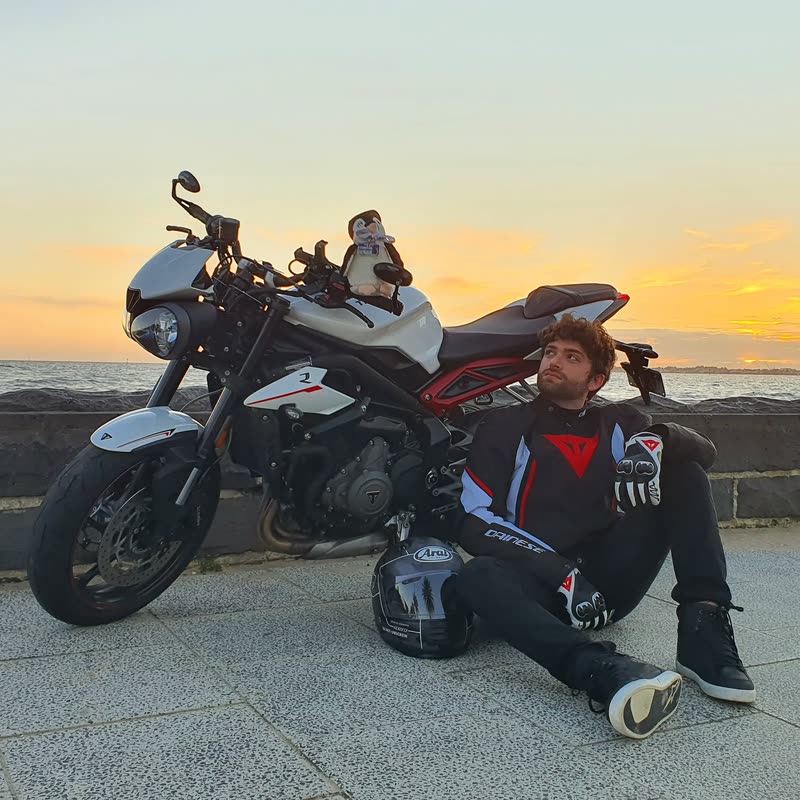 Damiano sitting on the ground beside a motorcycle at sunset